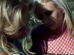 Katie Gold and Hillary Scott kiss each other sensually outdoors. They are sitting on a car parked near the street when they expose their tits and pussies.