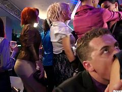 Playful brunette chics kneels down in front of kinky dudes during corporate party celebration to mouth fuck their hard cocks in sultry group sex video by Tainster.