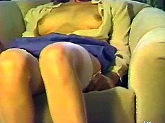 Curly brunette chick sits on a armchair. She lifts her skirt up and starts to finger her bushy vagina in retro video.
