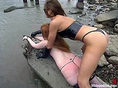 Submissive redhead girl gets humiliated by the brunette on the rocky shore. Neeka strips the clothes off and then gets spanked painfully.