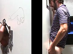 A dude pulls down jeans and pushes his dick through a hole in a wall. This bearded guy gets his dick sucked by another dude.