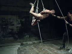 This gay slave hunk is tied up in rope and the master has hanged him from the ceiling. The slave has rope tightly wrapped around his cock and ball and the master give the rope a tug. This makes the gay slave sway back and forth.